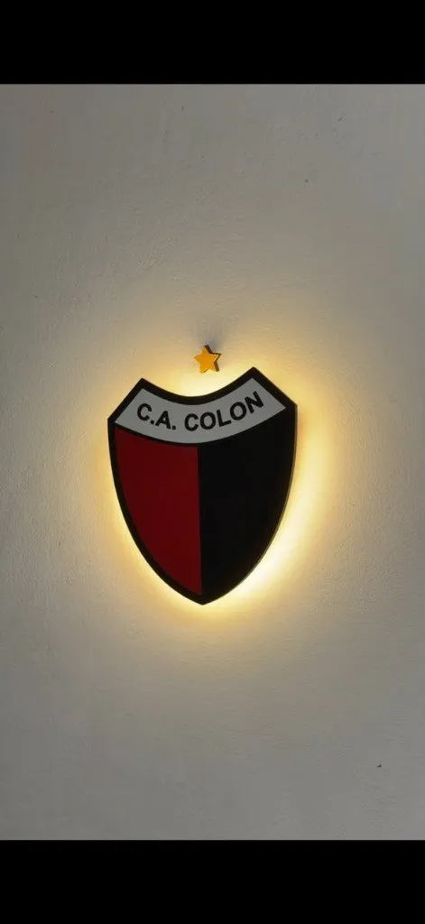 Escudo de Colón en madera, retroiluminado sobre una pared blanca